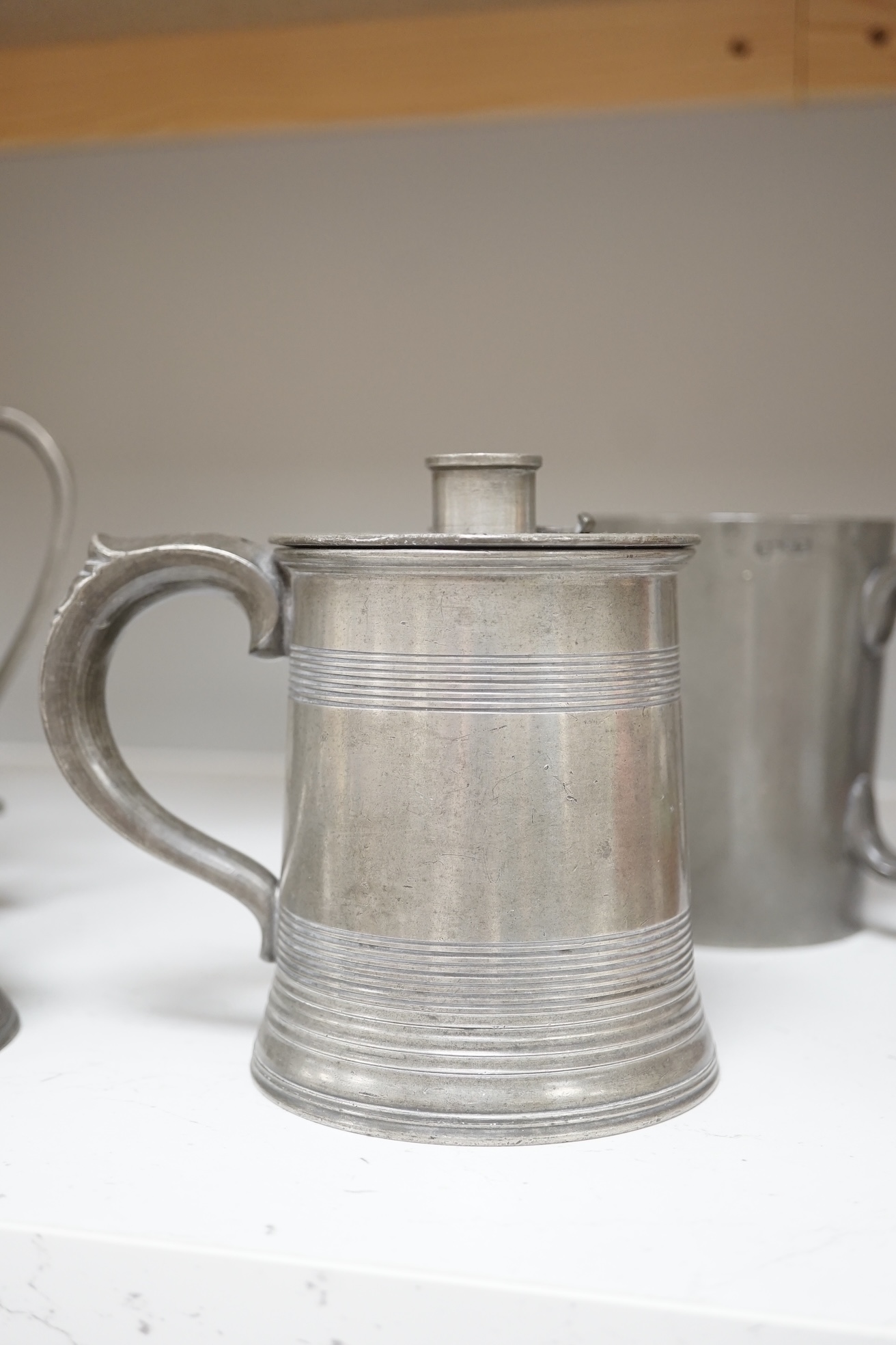 Six items of 18th century and later pewter including a jug, candlesticks, a pint measure, and a bronze hand bell, 24cm high. Condition - fair.